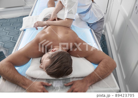Man lies on couch while woman therapist does back massage with elbow in hospital office 89423705