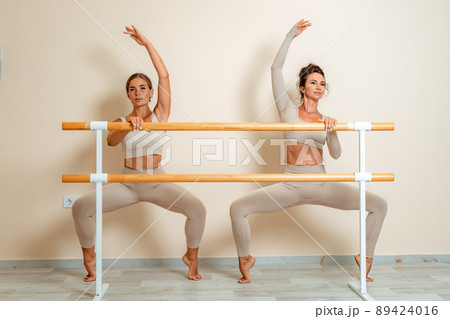 Near the barre, in the choreographic hall, two women in a beige top and leggings are engaged. 89424016