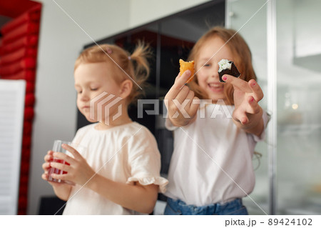 Two little girls siblings having fun and eating on the kitchen at home with japanese food. 89424102