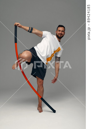 A fighter in white t-shirt and black shorts, stands in a fighting artificially pose and holds a fight stick on studio background. A fighter in white t-shirt and black shorts, stands in a fighting artificially pose and holds a fight stick on studio background. 89424185