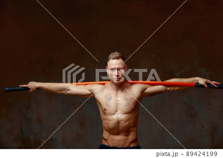 A fighter or karate man, stands in a fighting artificially pose and holds a bamboo stick on gray wall studio background. A fighter or karate man, stands in a fighting artificially pose and holds a bamboo stick on gray wall studio background. 89424199