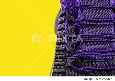 Lacing of purple black textile sneakers against yellow background.  89425507