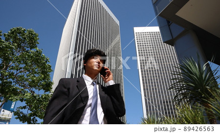 アメリカ、ロサンゼルスのダウンタウンを歩きながら電話する日本人ビジネスマン 89426563