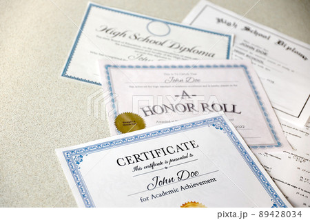 A honor roll recognition, certificate of achievement and high school diploma lies on table. Education documents 89428034