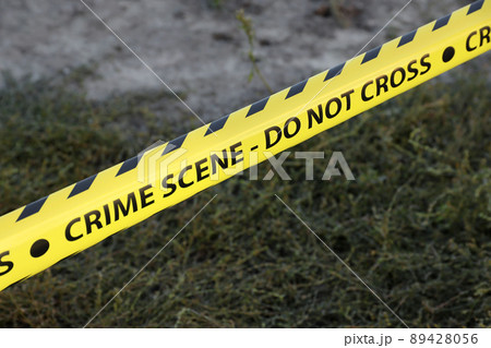 Crime scene tape for covering the area cordon. Yellow tape with blurred forensic law enforcement background in cinematic tone 89428056