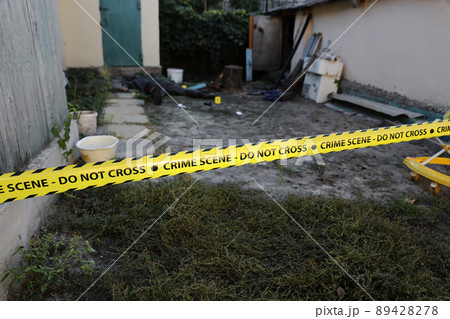 Victim of a violent crime in a backyard of residental house in evening. Dead man body under the yellow police line tape and evidence markers on crime scene 89428278