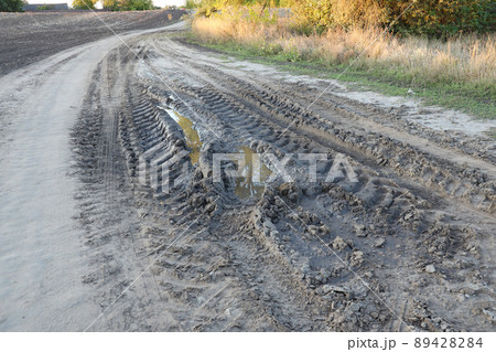 Autumn landscape with a curved road and traces of the tread of large wheels of agricultural machinery Autumn landscape with a curved road and traces of the tread of large wheels of agricultural machinery 89428284