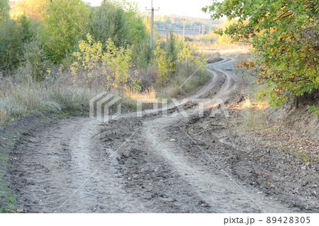 Autumn landscape with a curved road and traces of the tread of large wheels of agricultural machinery 89428305