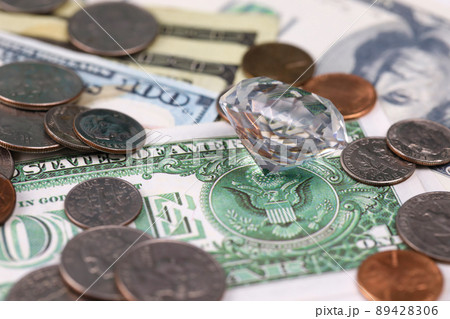 US money bills and coins with large diamond close up. Big amount of dollars and huge transparent gem on table. Business and jewellery 89428306