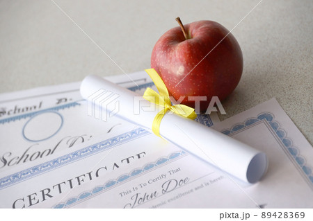 A honor roll recognition, certificate of achievement and high school diploma lies on table with small scroll and red apple. Education documents 89428369