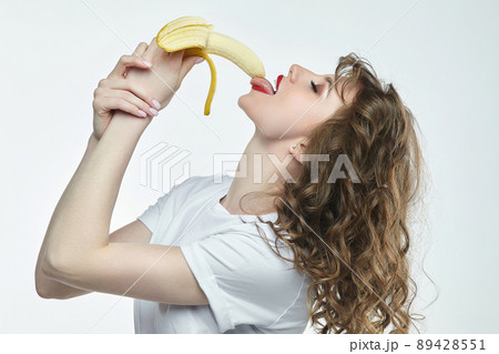 cheerful girl with red lipstick licks a banana with her tongue 89428551