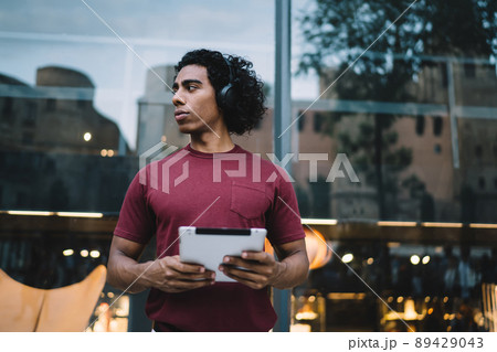 Hipster guy in bluetooth earphones pondering on audio book 89429043