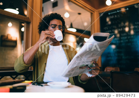 20s pensive man in trendy wear reading newspaper on break 89429473