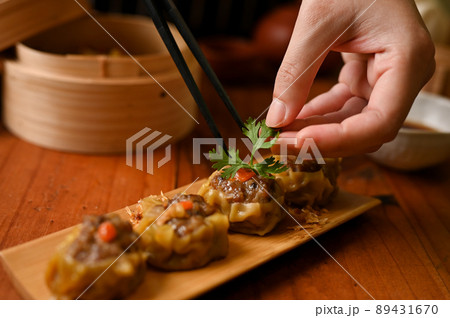 Female chef using chopsticks, garnishing steamed pork or meat dumplings with coriander leaf. Female chef using chopsticks, garnishing steamed pork or meat dumplings with coriander leaf. 89431670