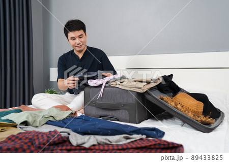 man preparing and packing clothes into suitcase on bed at home, holiday travel concept man preparing and packing clothes into suitcase on bed at home, holiday travel concept 89433825
