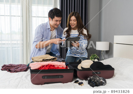 couple writing tablet and packing clothes into suitcase on bed at home, planning travel holiday. couple writing tablet and packing clothes into suitcase on bed at home, planning travel holiday. 89433826
