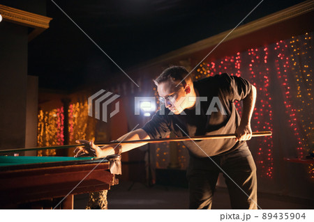 Entertainment concept. Concentrated young man in glasses playing billiard. Side view 89435904