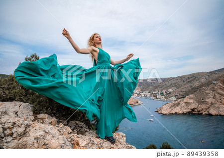 A woman in an emerald dress, a fashion model with long silk wings in a flowing dress, flying fabric on the embankment. A woman in an emerald dress, a fashion model with long silk wings in a flowing dress, flying fabric on the embankment. 89439358