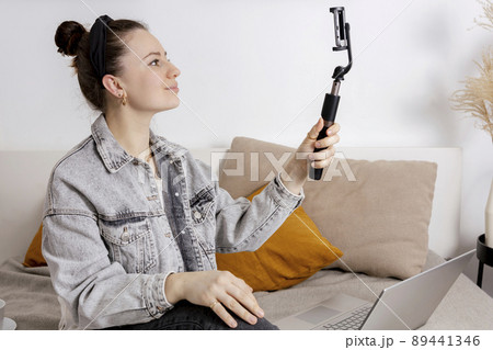 Young brunette woman making selfie on smartphone for her followers. Young influencer girl. Popularity in internet, friends online. Beautiful girl making content for her social media account. 89441346