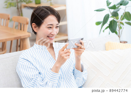 ソファーに座るミドル女性（スマホ・横向き・インターネット・動画鑑賞） 89442774