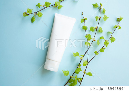 White Cream tube and birch branches with young small leaves on blue background. Cosmetic skincare product blank plastic package. White bottle of unbranded lotion, balsam, toothpaste mockup, flat lay. 89443944