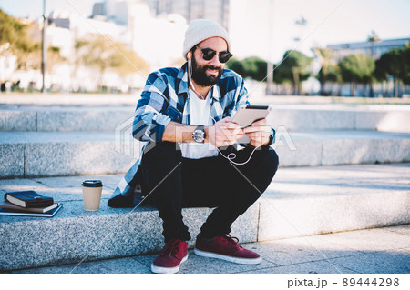 Turkish hipster guy in earphones and sunglasses watching video vlog via touch pad 89444298