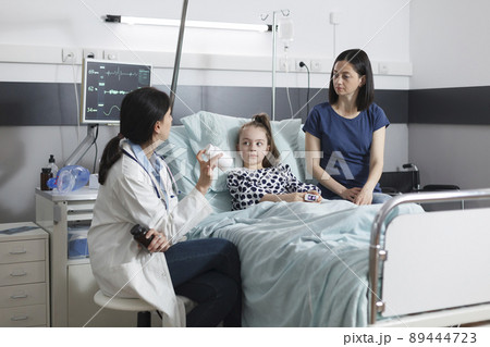 Clinic pediatric specialist recommending ill patient girl right medicine for illness remission. Hospital pediatrist specialist talking with attentive mother about illness treatment. 89444723