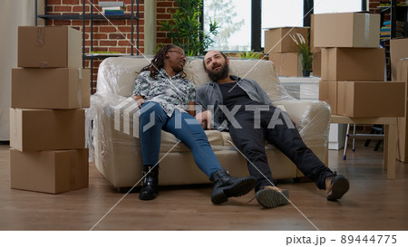 Multiethnic couple relaxing on sofa after unpacking furniture, preparing apartment space to move in together. Taking break on couch, decorating new rented home with belongings. 89444775