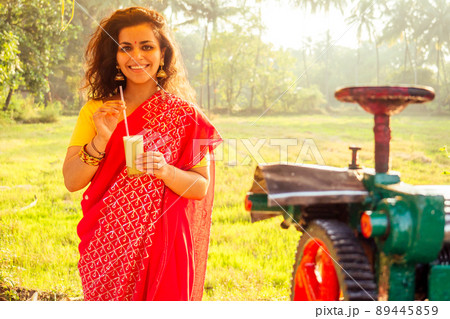 beautuful induan woman in red sari standing near sugarcane juice maker apparatus machine , plantation summer farm background. small business start up beautuful induan woman in red sari standing near sugarcane juice maker apparatus machine , plantation summer farm background. small business start up 89445859