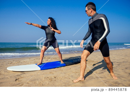 man instructor demonstrating how to stand up on surfboard to indian woman in surf class in Goa sea 89445878