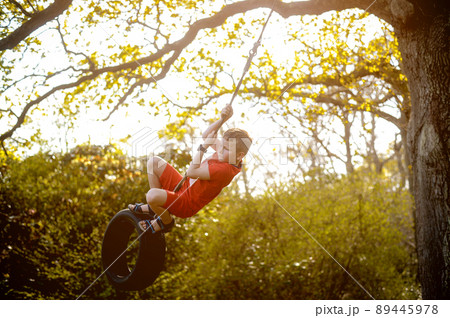 Happy child playing tire swing hanging at playground . Kids play on school or kindergarten yard. Active kid swing Healthy summer activity for children. Little boy swinging on rubber ring Happy child playing tire swing hanging at playground . Kids play on school or kindergarten yard. Active kid swing Healthy summer activity for children. Little boy swinging on rubber ring 89445978
