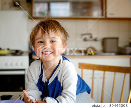 Happy smiling little kid having breakfast in the kitchen with cereal, milk and banana. Child boy likes to eat 89446008