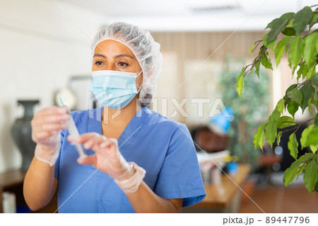 Female nurse wearing in face mask and medical uniform holding vial and syringe 89447796