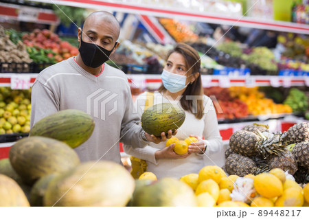 Husband and wife wearing protective masks picking ripe melon at a supermarket Husband and wife wearing protective masks picking ripe melon at a supermarket 89448217