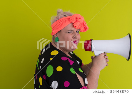 Funny plus size woman woman posing isolated on pastel green background studio portrait. People emotions lifestyle concept. Mock up copy space. Screaming in megaphone.  89448870