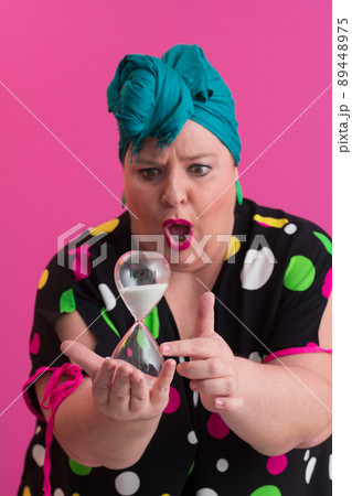 Portrait of plus size young lady smiling hands holds sand clock isolated on pink color background. Portrait of plus size young lady smiling hands holds sand clock isolated on pink color background. 89448975