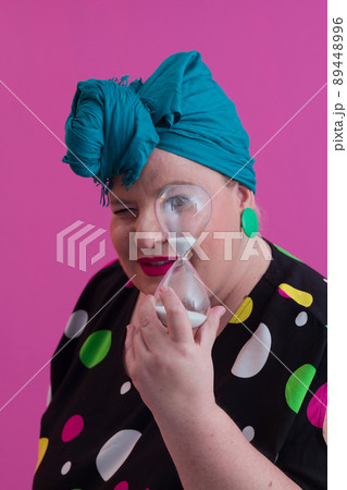 Portrait of plus size young lady smiling hands holds sand clock isolated on pink color background. Portrait of plus size young lady smiling hands holds sand clock isolated on pink color background. 89448996