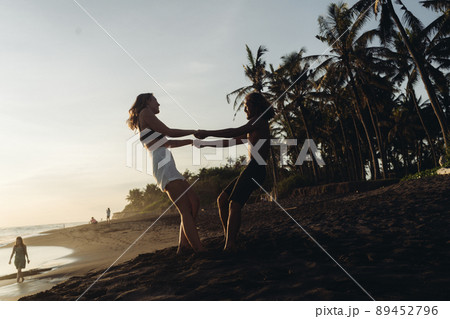 lovers clutching each other's hands whirling on the sand against the backdrop of the ocean and palm trees lovers clutching each other's hands whirling on the sand against the backdrop of the ocean and palm trees 89452796