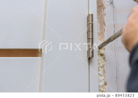Carpenter at installing interior wood door installation working with mounting foam 89453823