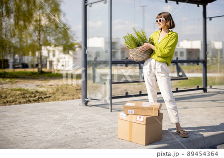 Woman with parcels and flowerpot on a bus stop Woman with parcels and flowerpot on a bus stop 89454364
