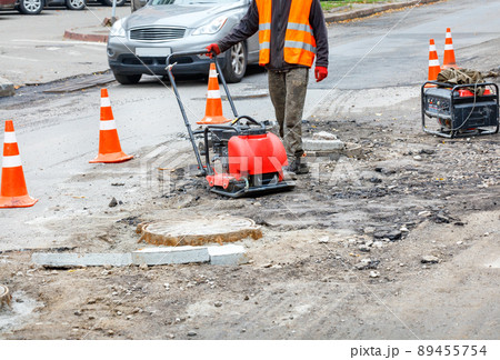 A road service worker repairs a section of the carriageway near a sewer manhole. 89455754