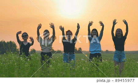 Girls friends waving their hands to the setting sun on the background of the sunset. Girls friends waving their hands to the setting sun on the background of the sunset. 89455977