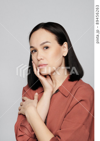 Portrait of serious young Asian woman with natural makeup touching own face against white background Portrait of serious young Asian woman with natural makeup touching own face against white background 89456263