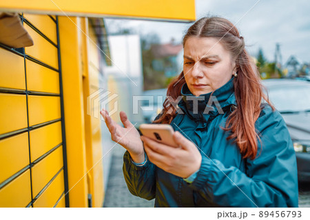 Caucasian angry woman with smartphone app at outdoor automated parcel machine. Mail delivery and post service concept 89456793