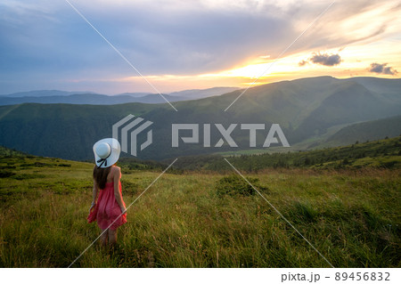 Young woman in red dress standing on grassy field on a windy evening in autumn mountains enjoying view of nature. Young woman in red dress standing on grassy field on a windy evening in autumn mountains enjoying view of nature. 89456832