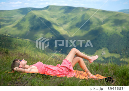 Young woman in red dress lying down on green grassy meadow on a warm sunny day in summer mountains enjoying view of nature. Young woman in red dress lying down on green grassy meadow on a warm sunny day in summer mountains enjoying view of nature. 89456834