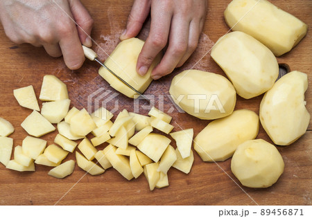 Woman's hand with a knife cutting slicing potatoes on wooden board in kitchen. Healthy eating and lifestyle. View from above close-up 89456871