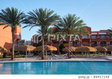 Empty deck chairs under straw shade umbrellas on swimming pool side in tropical resort. Summer vacations and getaway concept Empty deck chairs under straw shade umbrellas on swimming pool side in tropical resort. Summer vacations and getaway concept 89457149