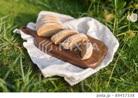 Composition of homemade white flour bread on wood board with white cloth napkin on the green grass . High quality photo 89457338