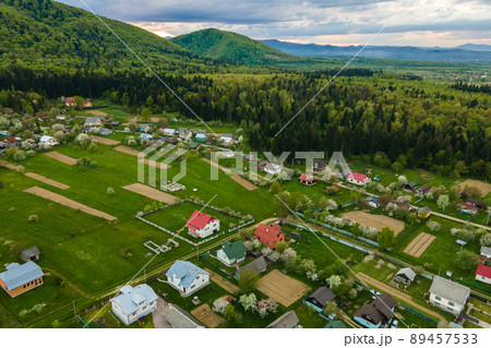 Aerial landscape view of village houses and distant green cultivated agricultural fields with growing crops on bright summer day 89457533